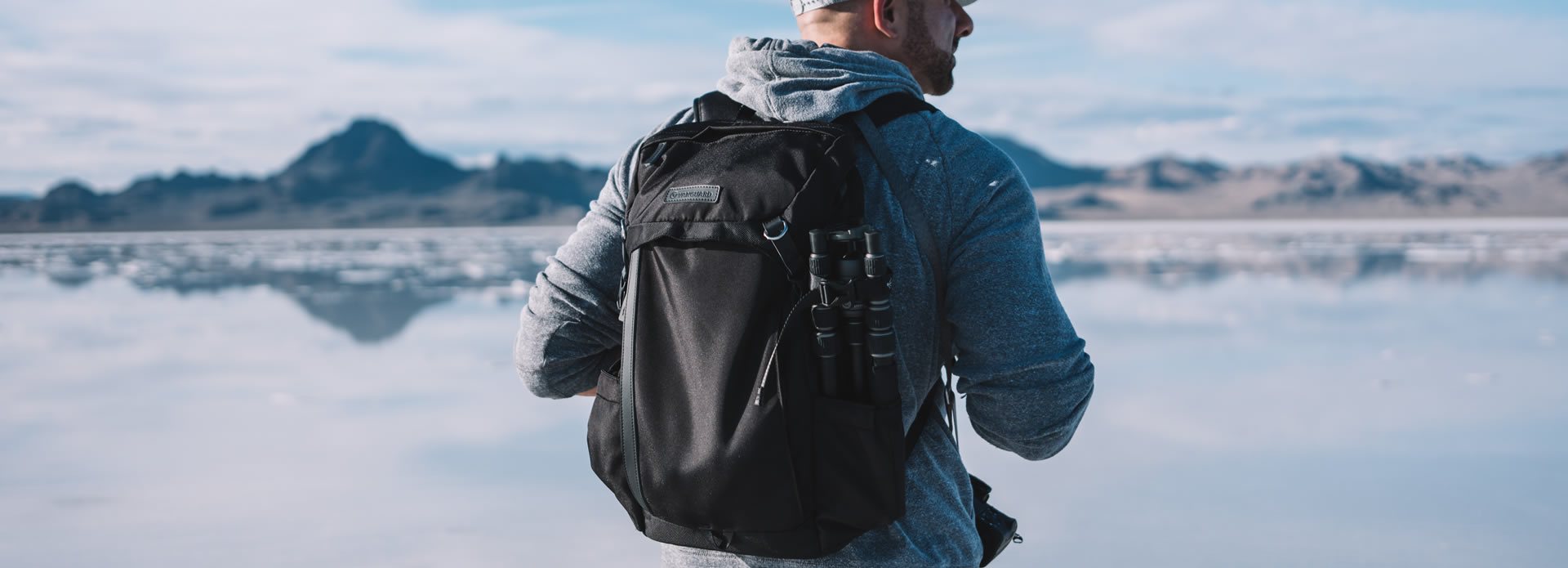 Fotógrafo en un paisaje natural con su mochila y trípode, en el fondo un lago y montañas