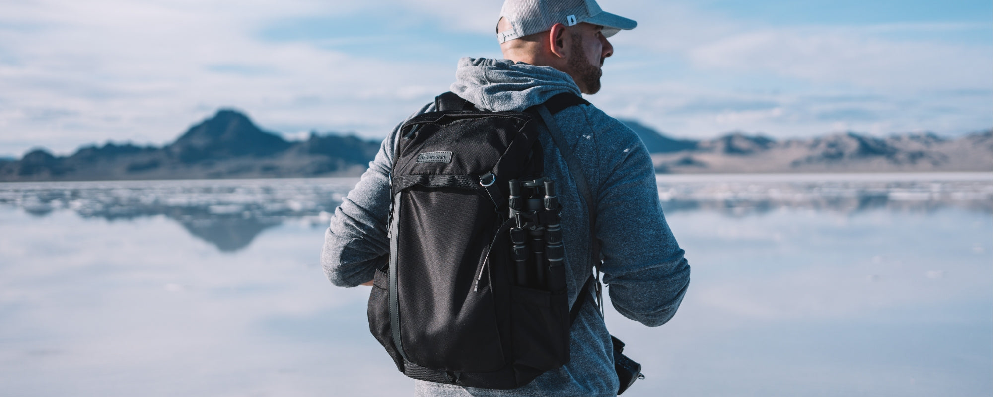 Fotógrafo con su mochila de cámara y trípode en la espalda sobre un fondo montañoso