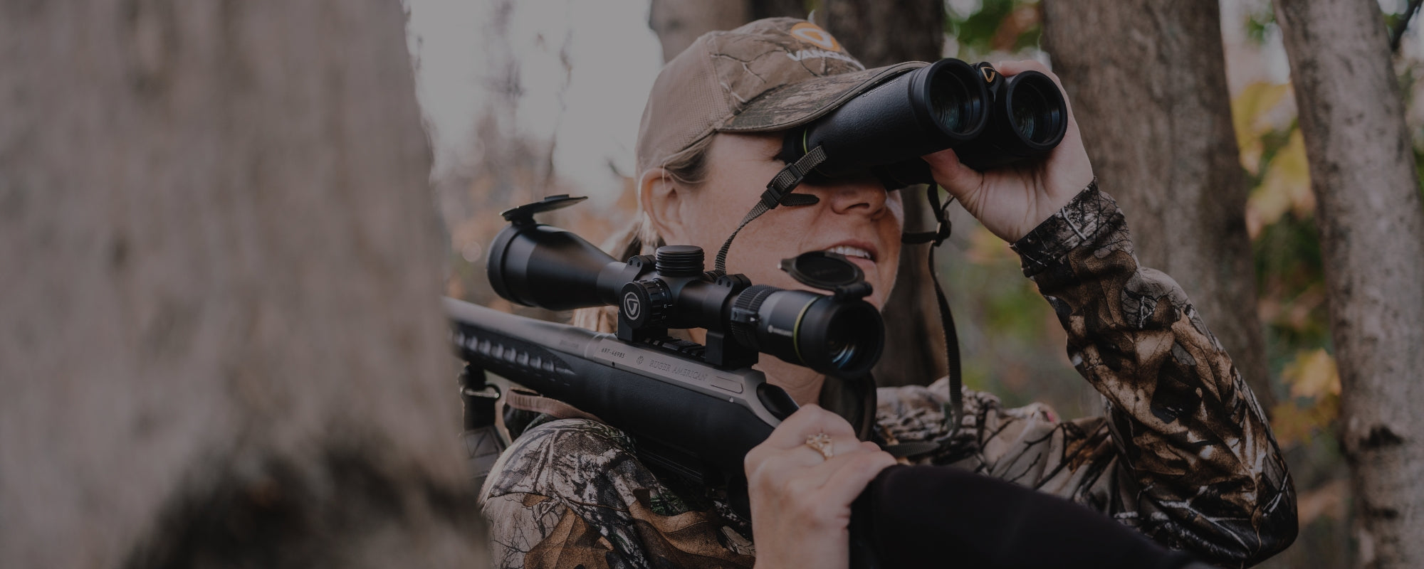 Mujer cazadora con rifle y visor observando con unos prismáticos