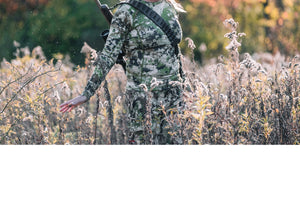 Cazadora con una correa para rifle y rifle caminado por el campo